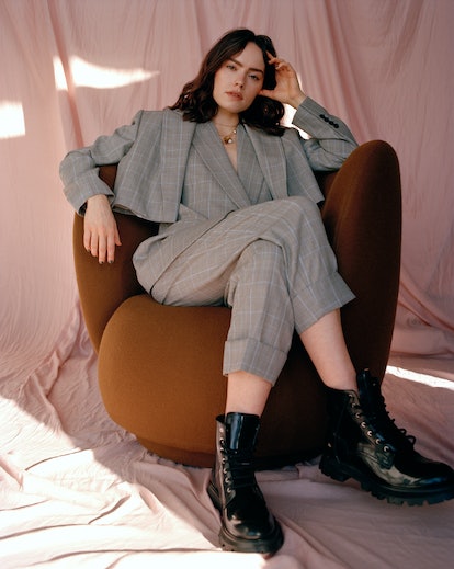 TZR cover star Daisy Ridley sitting down in a chair while wearing a gray suit by Alexander McQueen